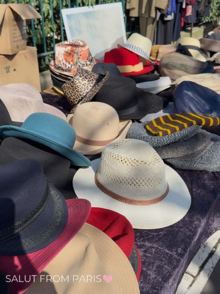 A colorful collection of vintage hats spread across a table at a Paris flea market. Straw felt patterned and brightly colored hats in red blue black and cream create an eclectic secondhand display.
