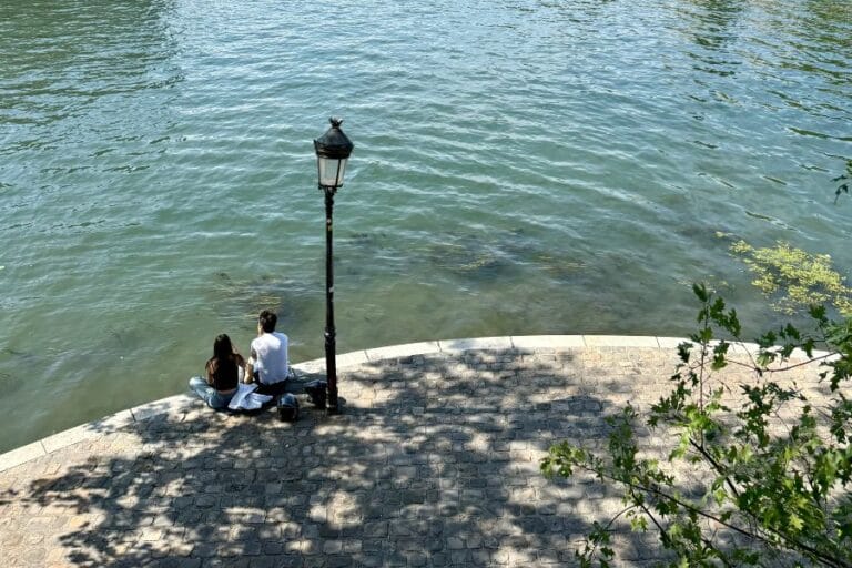 2 people sitting at the seine with a lamp post in
