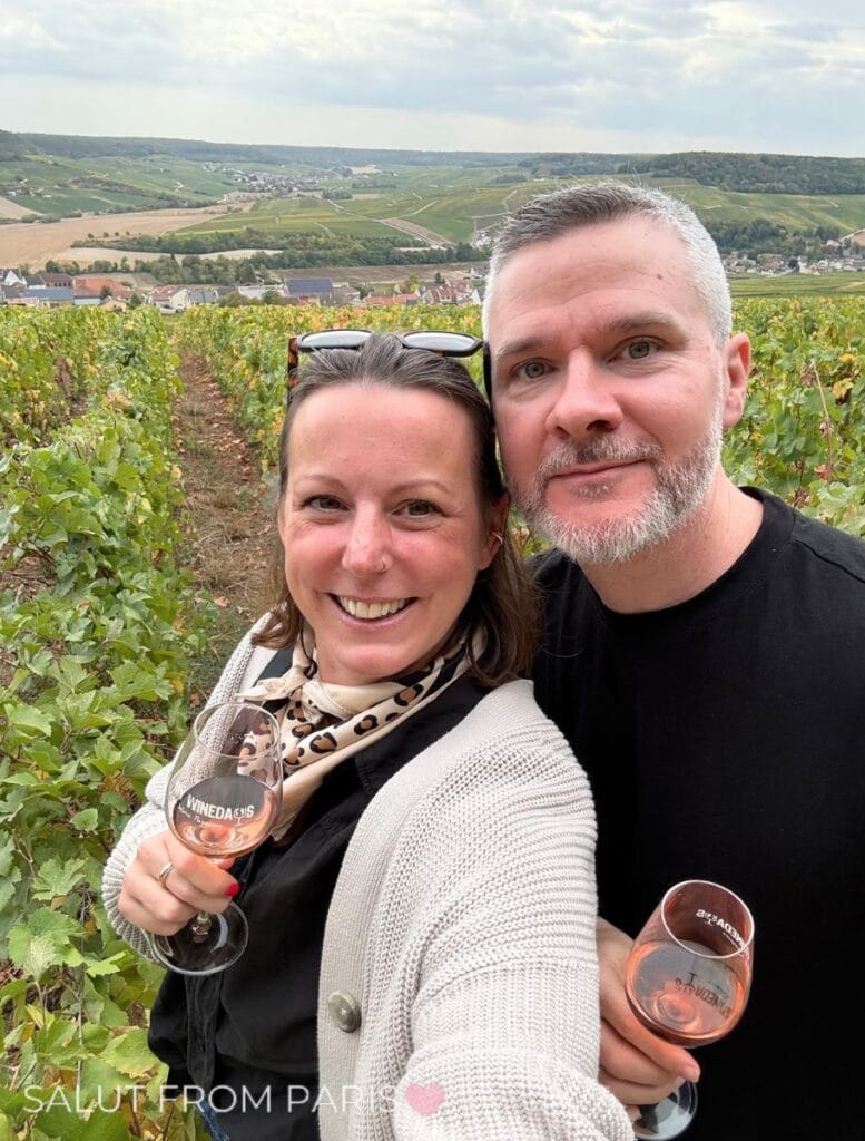 Lena and Laurent on a vineyard in Champagne holding a glass of rosé Champagne in their hand.
