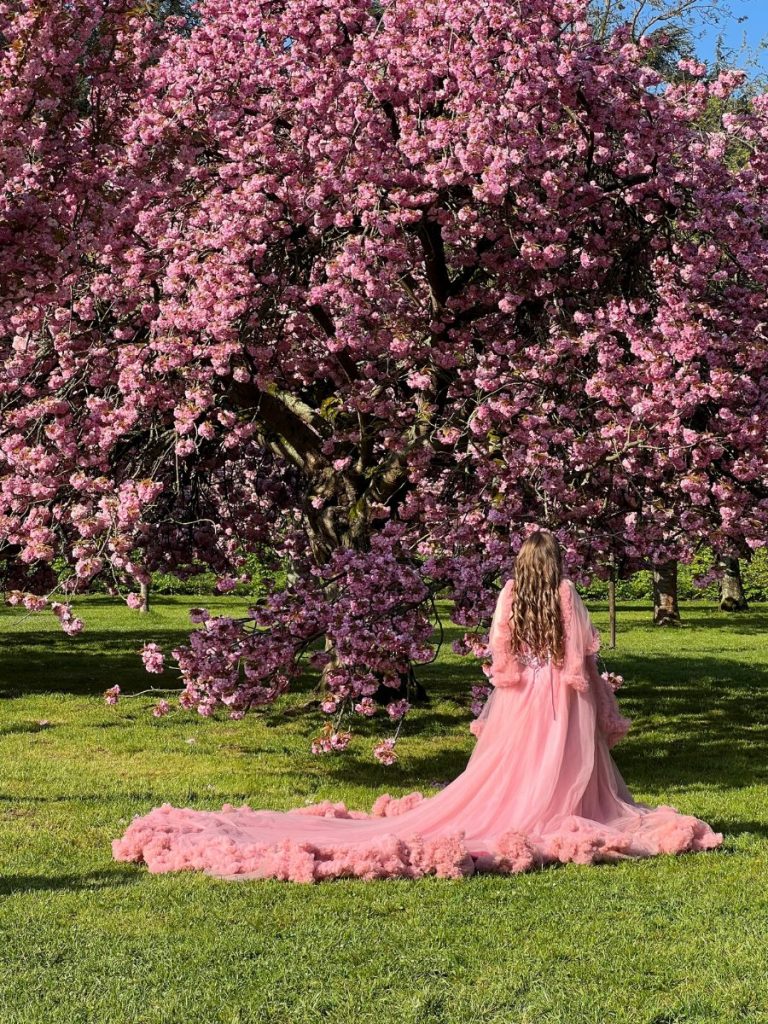woman in pink dress standing in front of a cherry blossom tree