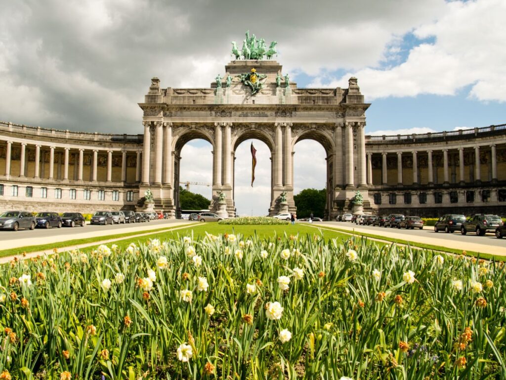 The grand triumphal arch at Parc du Cinquantenaire in Brussels rises above colorful spring flowers and manicured lawns. Majestic columns curve on either side, showcasing classic European architecture. This landmark park is one of Brussels’ most impressive and photogenic sites.