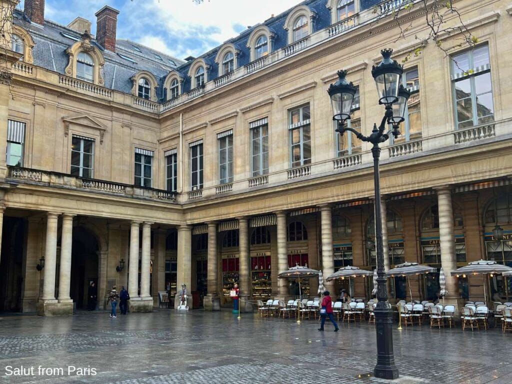 Cafรฉ Namours at the Palais Royal with a Parisian Lamp in the foreground and a terrasse with chairs and tables in the back
