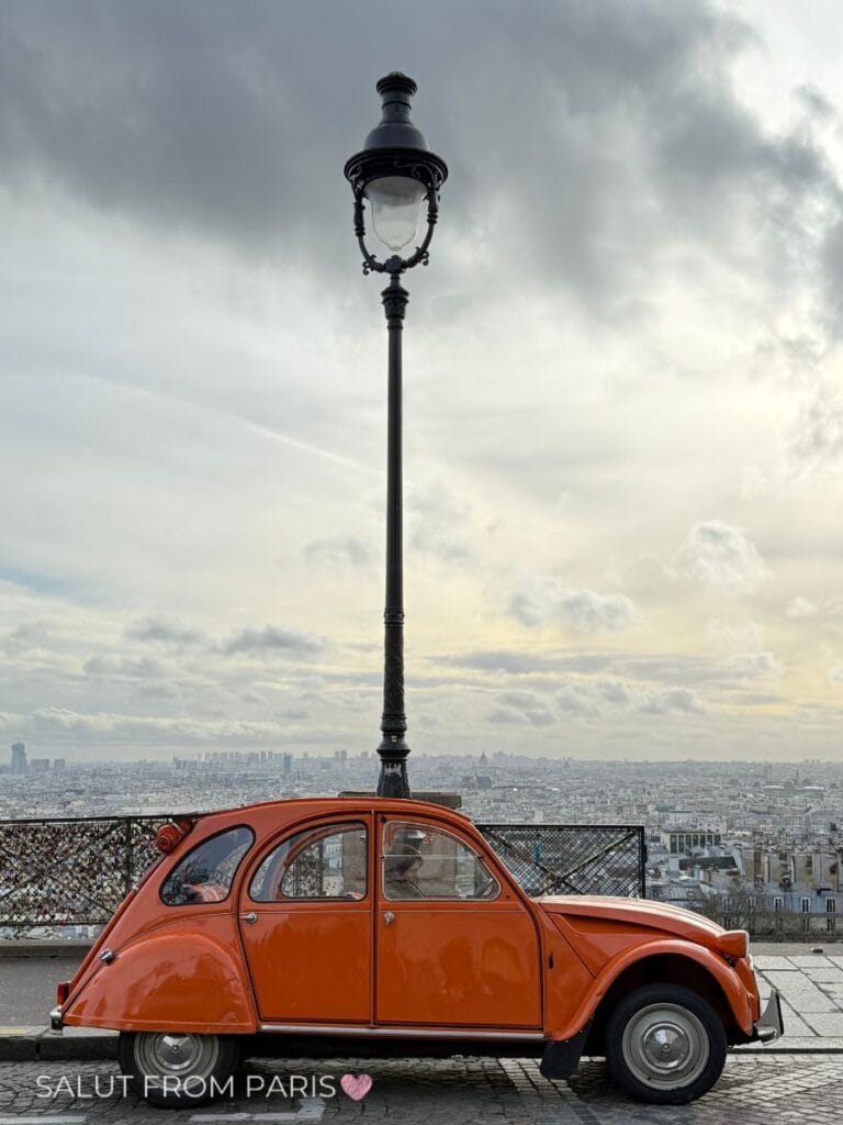 Vintage orange Citroën 2CV parked at Montmartre viewpoint, overlooking Paris on a cloudy winter day